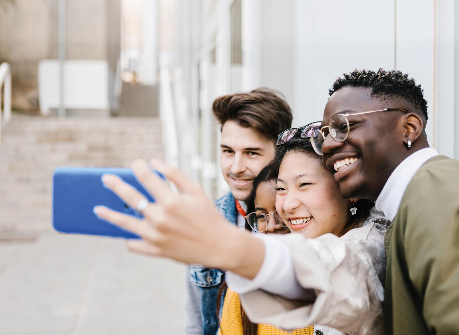Young adult woman taking selfie portrait with group of friends outdoors at school