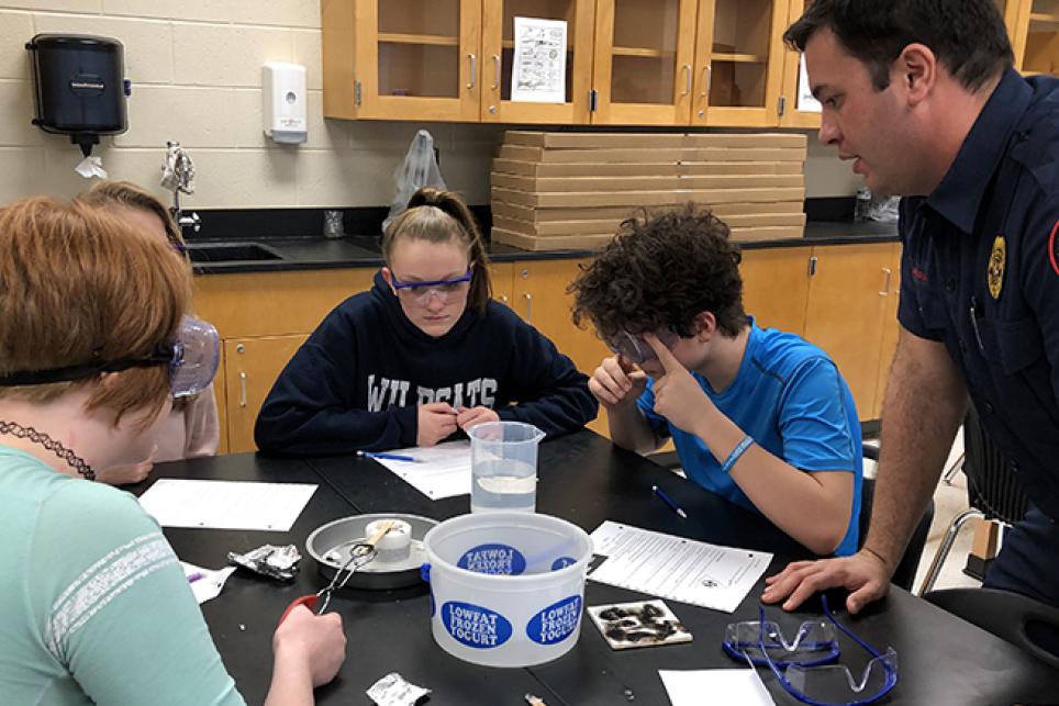 A Cobb County, Ga. firefighter assists Cobb County School District students as they learn about the fire triangle in the fire forensics Xplorlabs module.