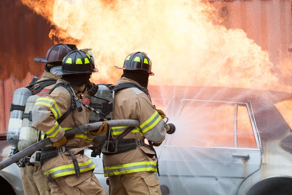 firefighters attacking a car fire with a fire hose