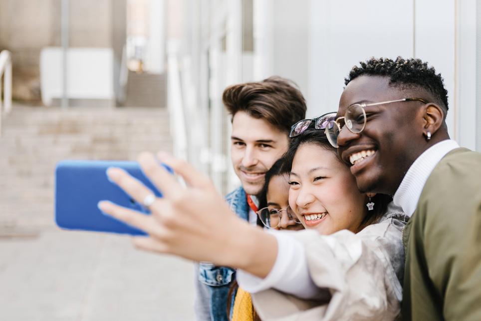 Young adult woman taking selfie portrait with group of friends outdoors at school