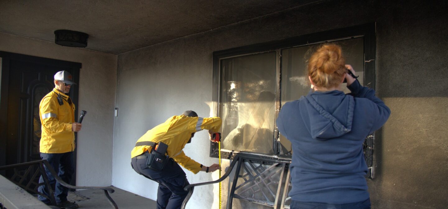 two men and one woman inspecting and photographing a fire damaged window