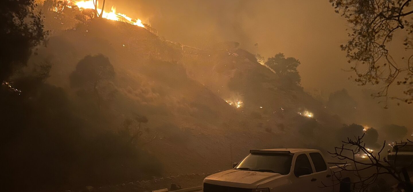 Wildfires approach the built environment, igniting vehicles.