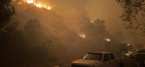 Wildfires approach the built environment, igniting vehicles.