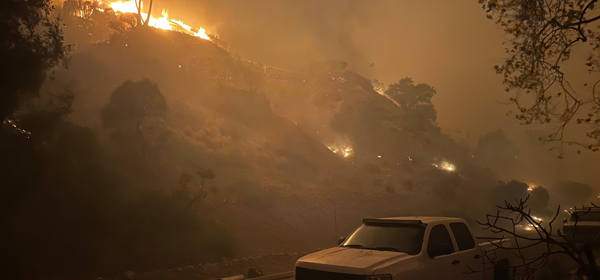 Wildfires approach the built environment, igniting vehicles.