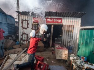 Residents of an informal settlement try to fight a fire on their own with limited resources before it spreads to neighboring vulnerable structures.