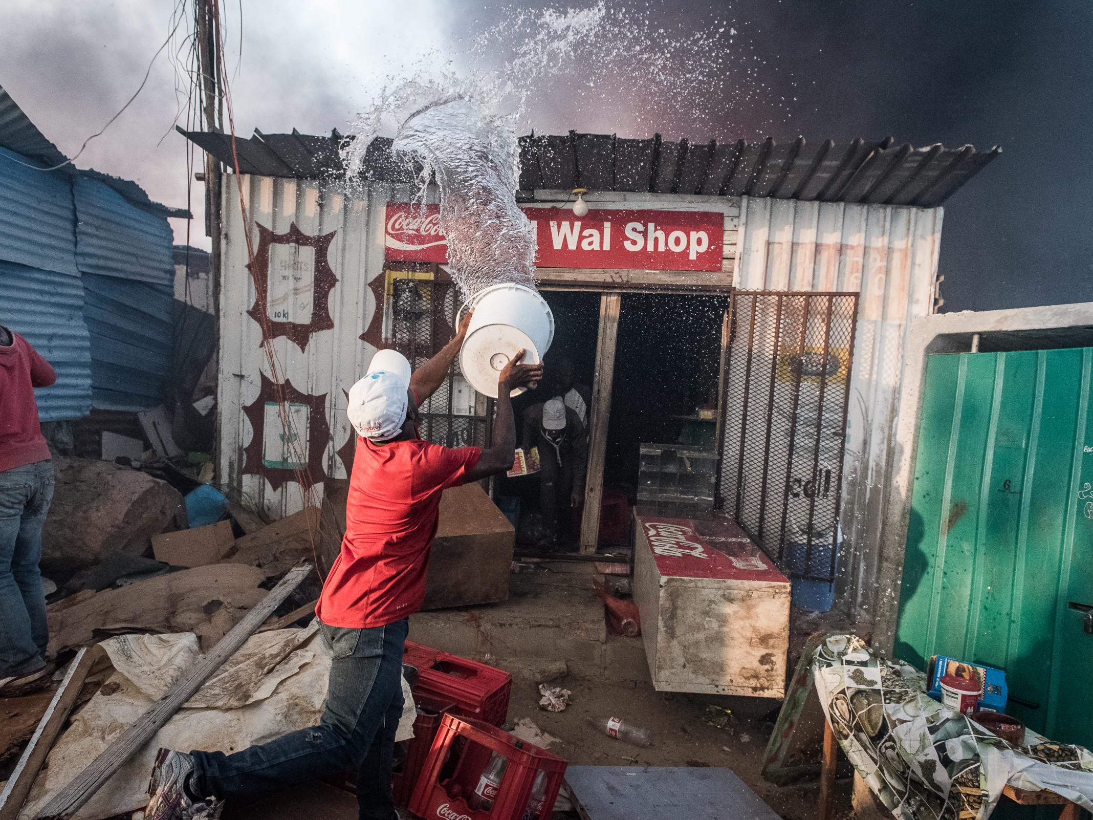 Residents of an informal settlement try to fight a fire on their own with limited resources before it spreads to neighboring vulnerable structures.